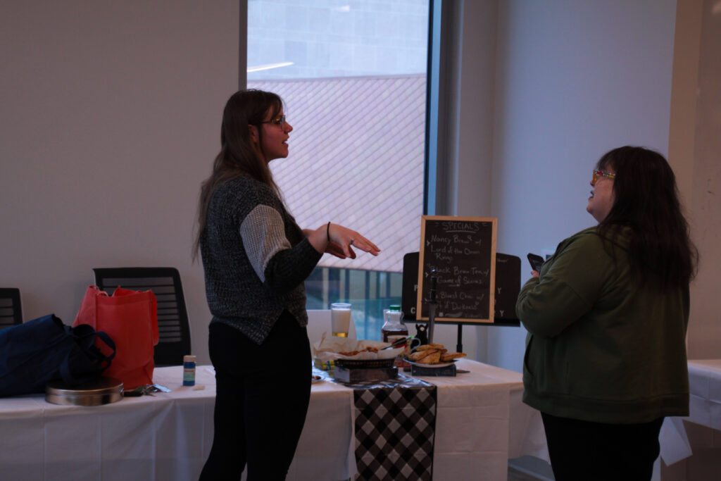 Two attendees speaking while standing in front of The Inkwell Daily Specials display.