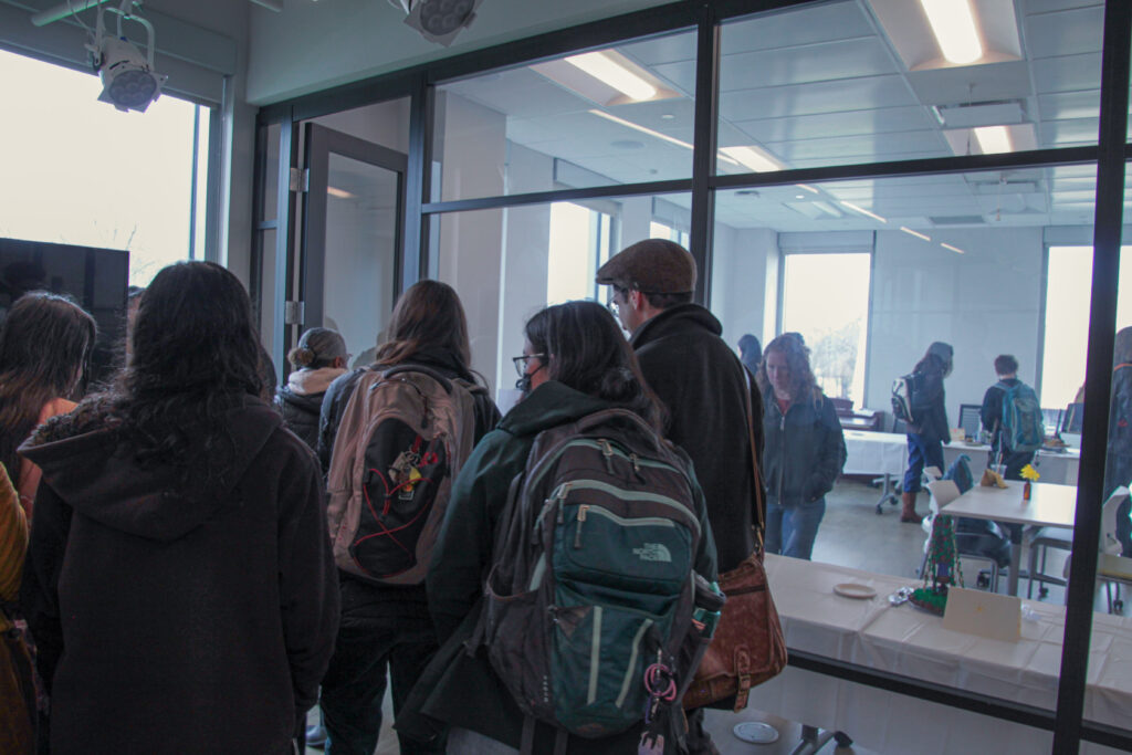 Group of attendees entering a room for the festival, a view of the room visible through a glass panel wall.