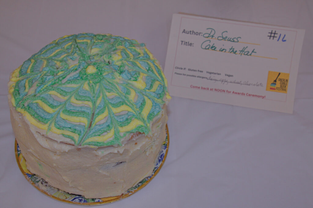 Circular cake with white frosting on edges and intricate pattern of yellow, green, and blue on top.