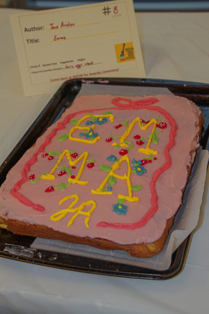Rectangular dessert decorated like a book cover with Emma and JA written in yellow frosting on pink frosting background.
