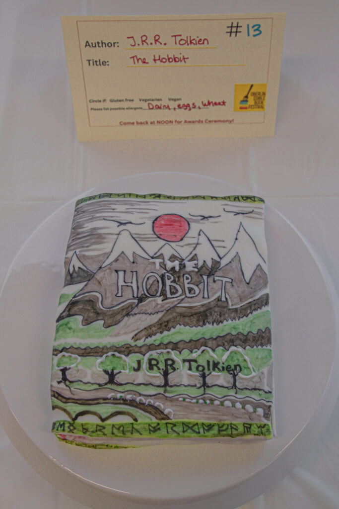 Rectangular dessert decorated like a book cover, with mountains, plains, and a sun, as well as text of the title and author.