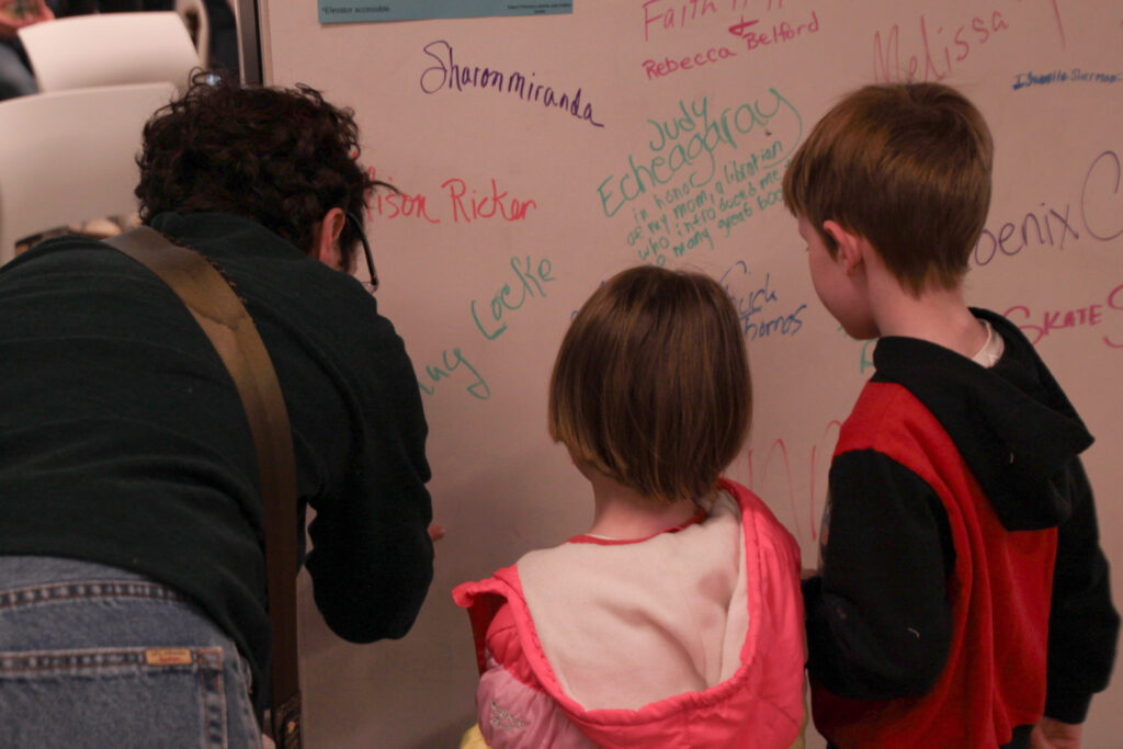 Attendee and two children standing at whiteboard while the attendee signs it.