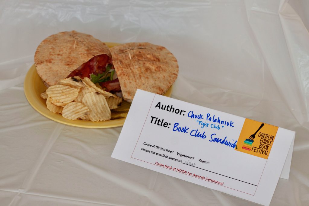 Photo of submission titled, "Book Club Sandwich" featuring a plate with a sandwich that includes bacon, and a side of potato chips