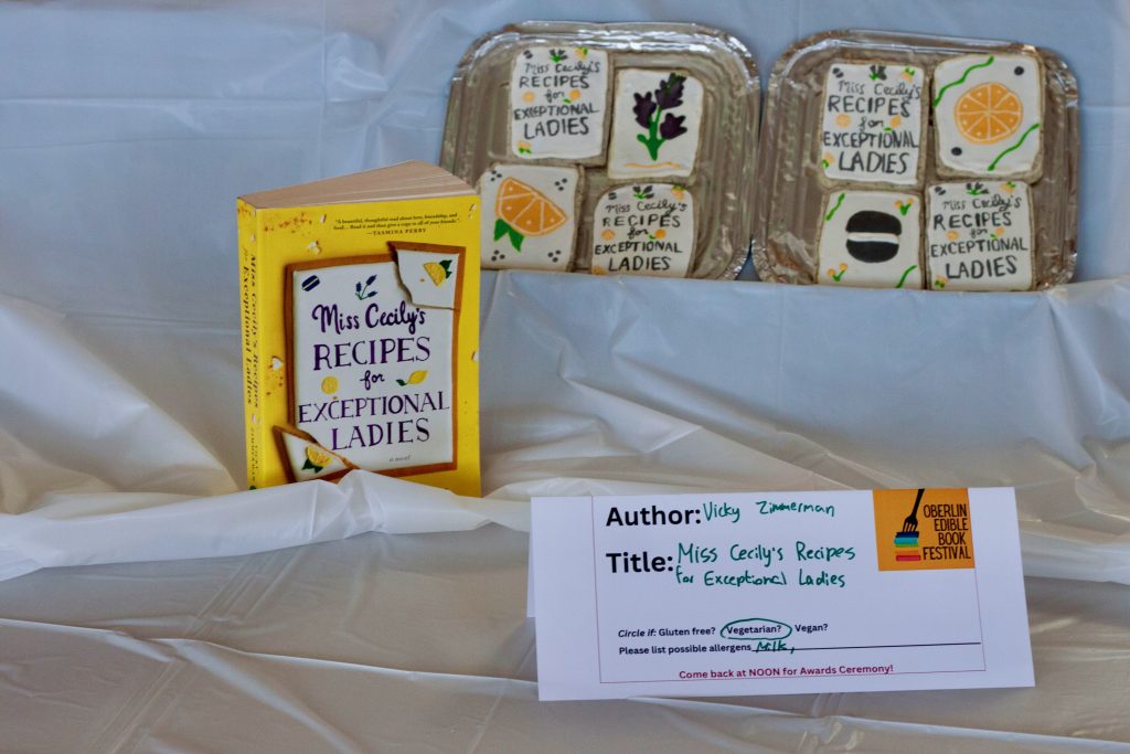 Photo of submission titled, "Miss Cecily's Recipes for Exceptional Ladies" featuring 8 iced cookies with decorations and the title of the book, and a copy of the book next to it