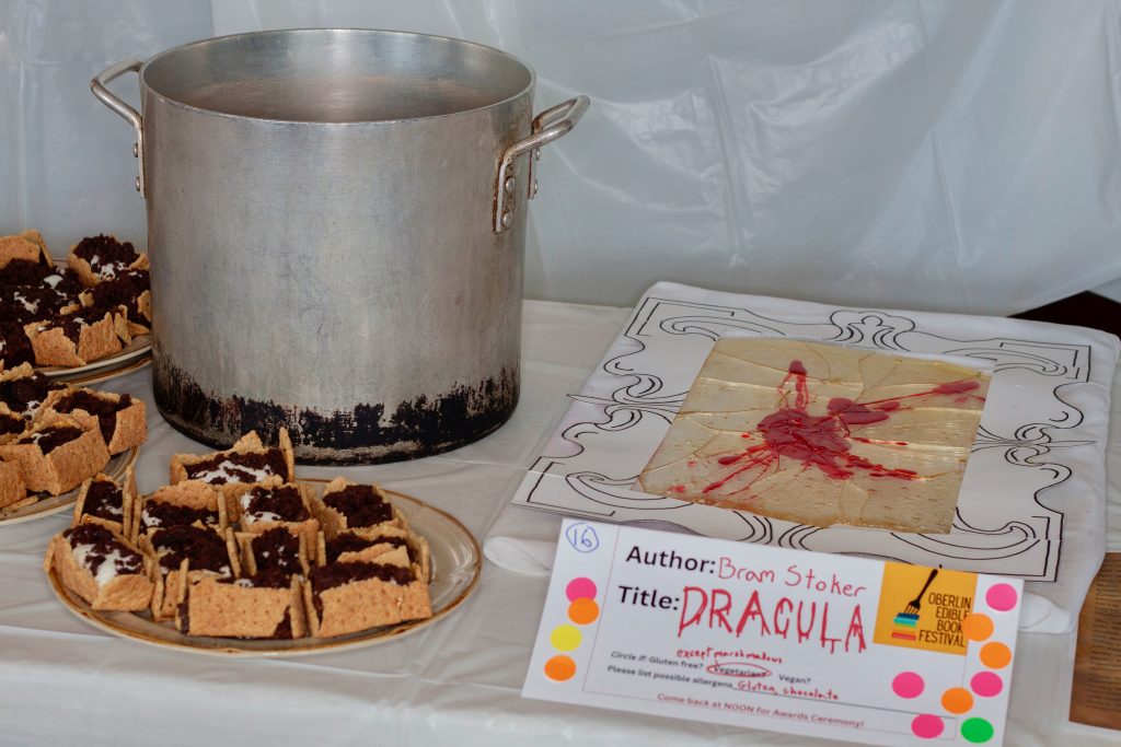 Photo of submission titled, "Dracula" featuring a desserts in the shape of coffins made of graham crackers and filled with cream and chocolate cookie crumbles resembling dirt, and a sheet of rock candy, shattered, with red splotches